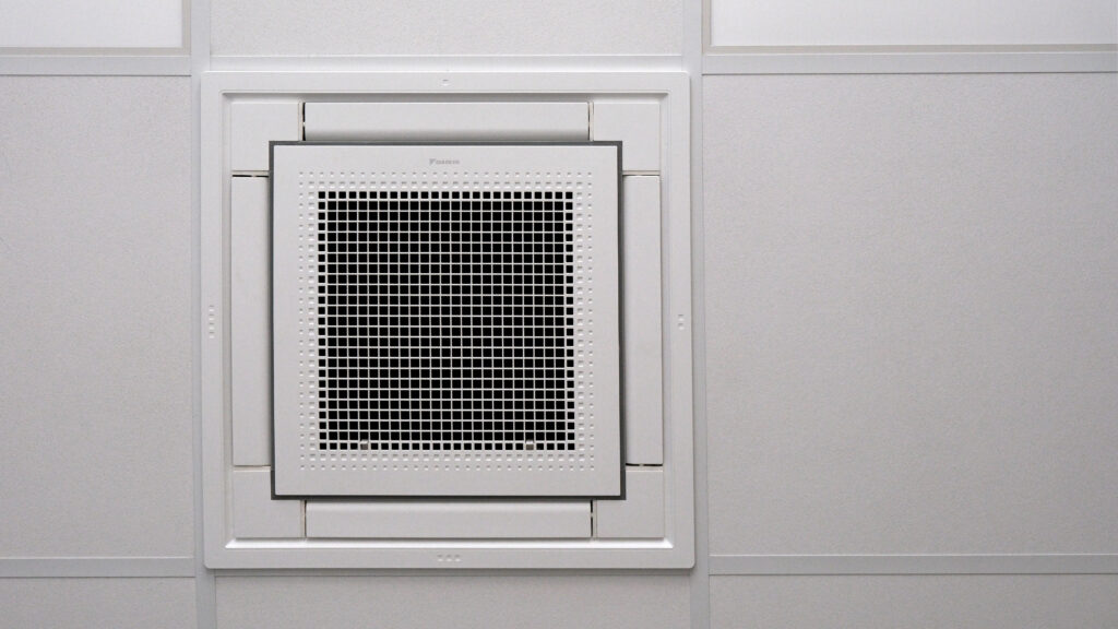 Quadratische Deckenkassette einer Klimaanlage mit zentralem Luftauslass in einer weißen Rasterdecke.