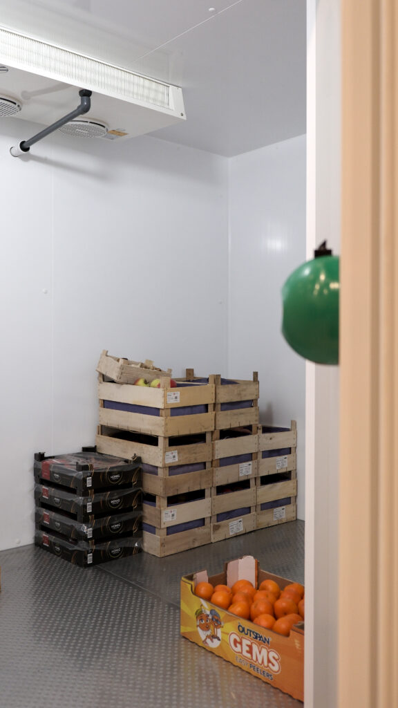 Kühlraum mit Obstkisten aus Holz und Karton, an der Decke ein Verdampfer für die Kälteanlage.