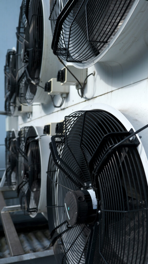 Reihe großer schwarzer Industrievemtilatoren mit Schutzgittern an einer weißen Kühlanlage im Außenbereich