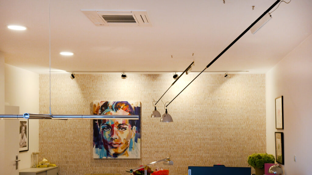 Innenraum mit Deckenklimaanlage, moderner Beleuchtung und farbigem Porträt an der Wand über einem Empfangsbereich